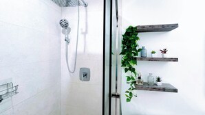 Un baño moderno con cabina de ducha de vidrio, cabezal de ducha de mano, grifo empotrado en la pared y una planta en maceta sobre un estante de madera.