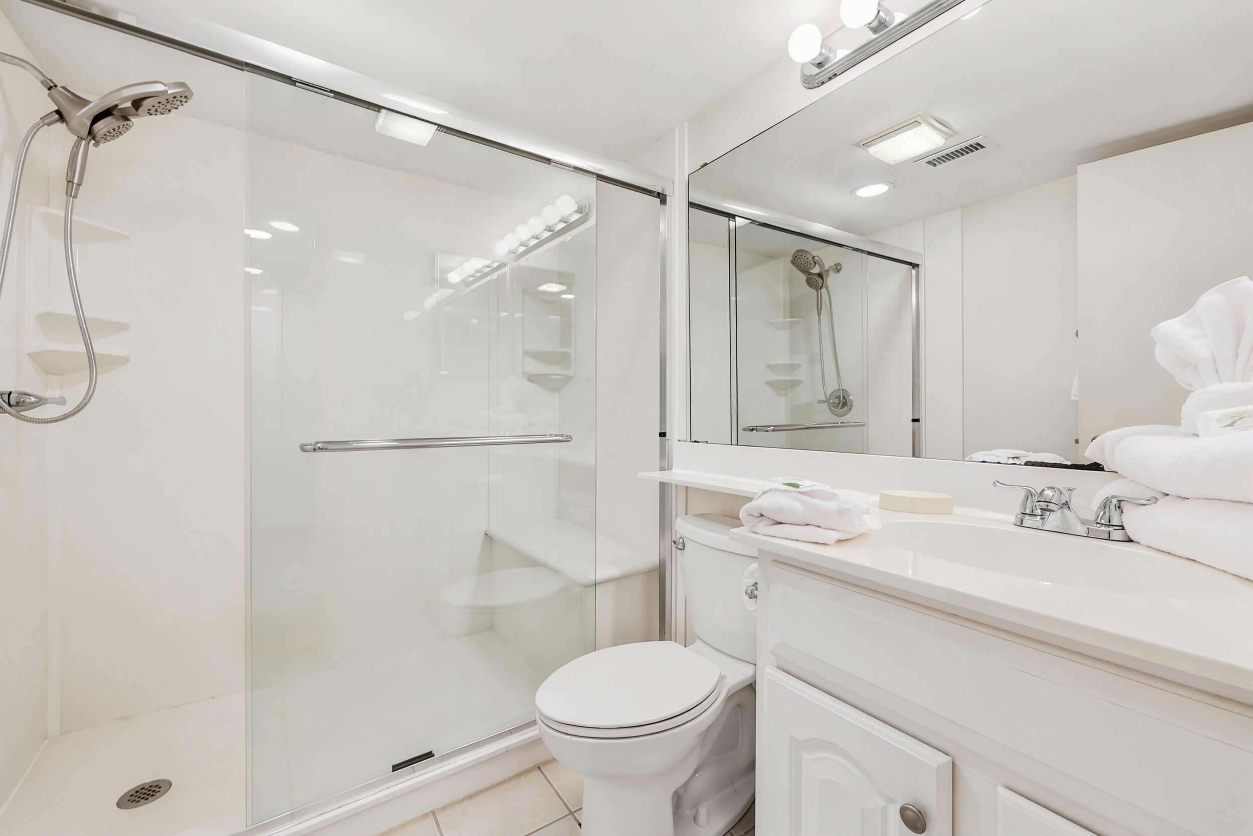Une salle de bain moderne avec une douche à parois de verre, des toilettes blanches et un meuble-lavabo avec un miroir.