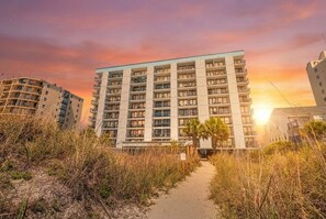 A multi-story hotel with a central courtyard, surrounded by tall buildings and a sunset sky. - Oceanfront Corner Unit-3BR Retreat at Waterpointe I (North Myrtle Beach)