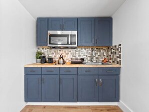 A compact kitchen with dark blue cabinets, a stainless steel microwave, a toaster, and a kettle on the countertop. - El Nido al Lago - 4 minutes to Raymond James Stadium (Tampa)