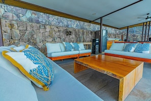 Uma sala de estar moderna com parede de pedra, mesa de centro de madeira e sofá com almofadas estampadas.