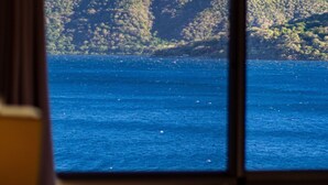 A room with a bed, a window, and a view of a body of water and hills.