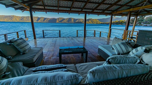 A covered outdoor seating area with a view of the water and mountains.