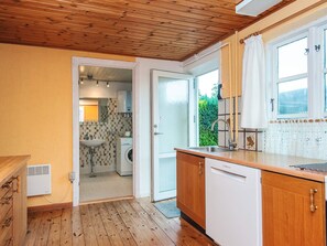 A kitchen with wooden cabinets, a Bosch dishwasher, and a window with lace curtains. - 6 Person Holiday Home in Odder (Odder)