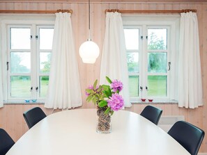 A dining area with a round table, chairs, a vase with flowers, and windows with curtains. - 6 Person Holiday Home in Odder (Odder)