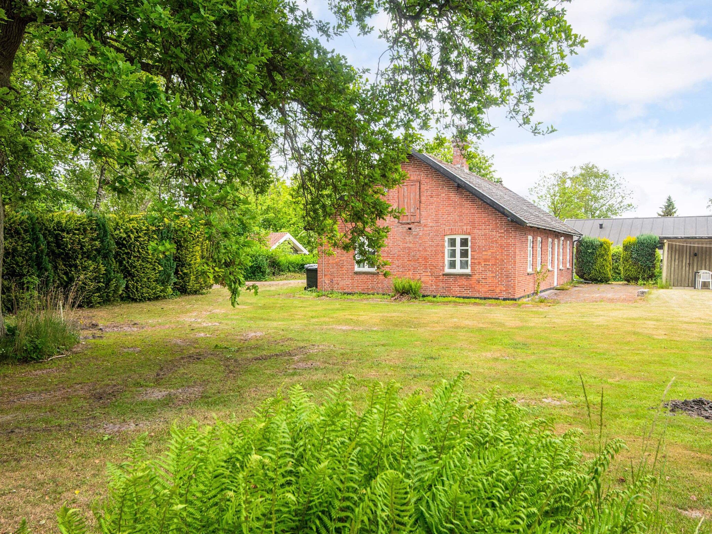 A brick house with a sloped roof, surrounded by a grassy yard and dense foliage.