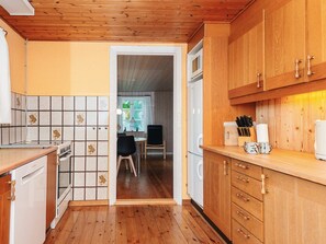 A kitchen with wooden cabinets, a tiled backsplash, and a view into a dining area. - 6 Person Holiday Home in Odder (Odder)