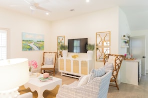 A living room with a TV, white furniture, and a painting. - The Lettie | Newly updated Coastal Cottage (St Simons Island)