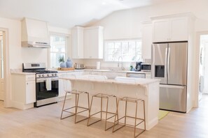 Una cocina moderna con muebles blancos, un refrigerador de acero inoxidable, una estufa a gas y una isla grande con taburetes.