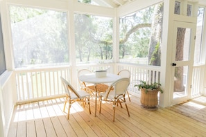 Une véranda avec une table ronde et des chaises, de grandes fenêtres et une clôture blanche en bois.