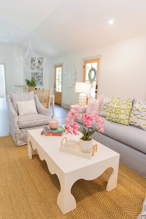 A living room with a white coffee table, a grey sofa, a white armchair, and a woven rug. - The Lettie | Newly updated Coastal Cottage (St Simons Island)