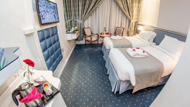 A hotel room with two beds, a small sitting area with a table and chairs, a TV mounted on the wall, and a decorative vase with flowers on the side table. - Montana Hotel Makkah (Makkah)