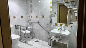 A modern bathroom with a shower, toilet, and sink, equipped with a handrail and grab bars for accessibility. - Montana Hotel Makkah (Makkah)
