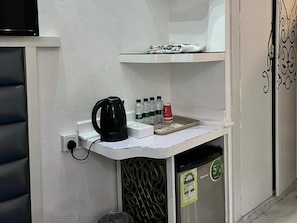 Et lille tekøkken med kaffemaskine, vandflasker og en skraldespand.