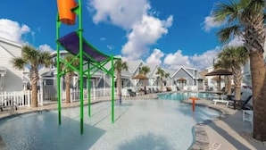 Un área de piscina con tobogán de agua, sillas de descanso y palmeras.