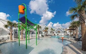 A pool area with a water slide, lounge chairs, and palm trees. -     Walk to Beach & Sandbox: Sleeps 6, Pool & Splash Pad (Corpus Christi)