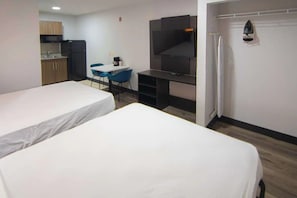 Ett hotellrum med två sängar, ett litet kök, ett skrivbord med en stol, en TV och en duschhörna.