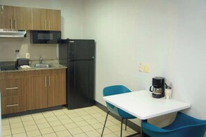 A compact kitchen with wooden cabinets, a black refrigerator, a microwave, a sink, a white table, and blue chairs. - Budget-Friendly Studio Close to Downtown West Palm Beach – 3 Miles (West Palm Beach)