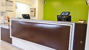 En receptionsdisk med en digital informationskiosk, ett golv belagt med marmorplattor och en grön vägg.