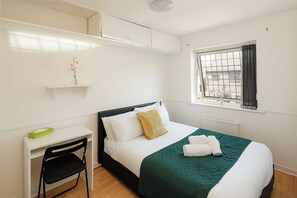 Ein Schlafzimmer mit Bett, Schreibtisch, Stuhl, Fenster mit Blick und Heizkörper.