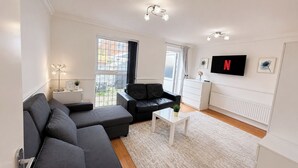 Moderni olohuone, jossa on kulmasohva, sohvapöytä, televisio ja ikkuna, josta on näkymä ulos.