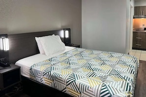 A hotel room with a bed, bedside tables, a nightstand, a headboard, and a kitchenette area.