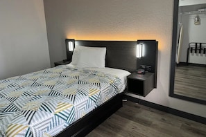 A hotel room with a bed, bedside tables, a nightstand, a wall-mounted TV, and a mirror.