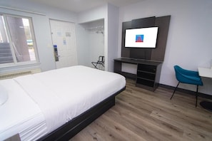 A hotel room with a bed, a TV mounted on the wall, a desk, and a chair.
