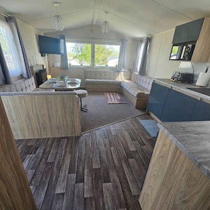 A compact living space with a kitchen, seating area, and a dining table. - 3BR Countryside Caravan up to 7 Guests (Tosside)
