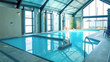 An indoor swimming pool with clear glass walls, a tiled floor, and a metal roof structure.