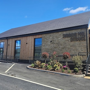 A building with a swimming pool entrance sign, a wooden facade, and a landscaped area with plants. - 3BR Countryside Caravan up to 7 Guests (Tosside)