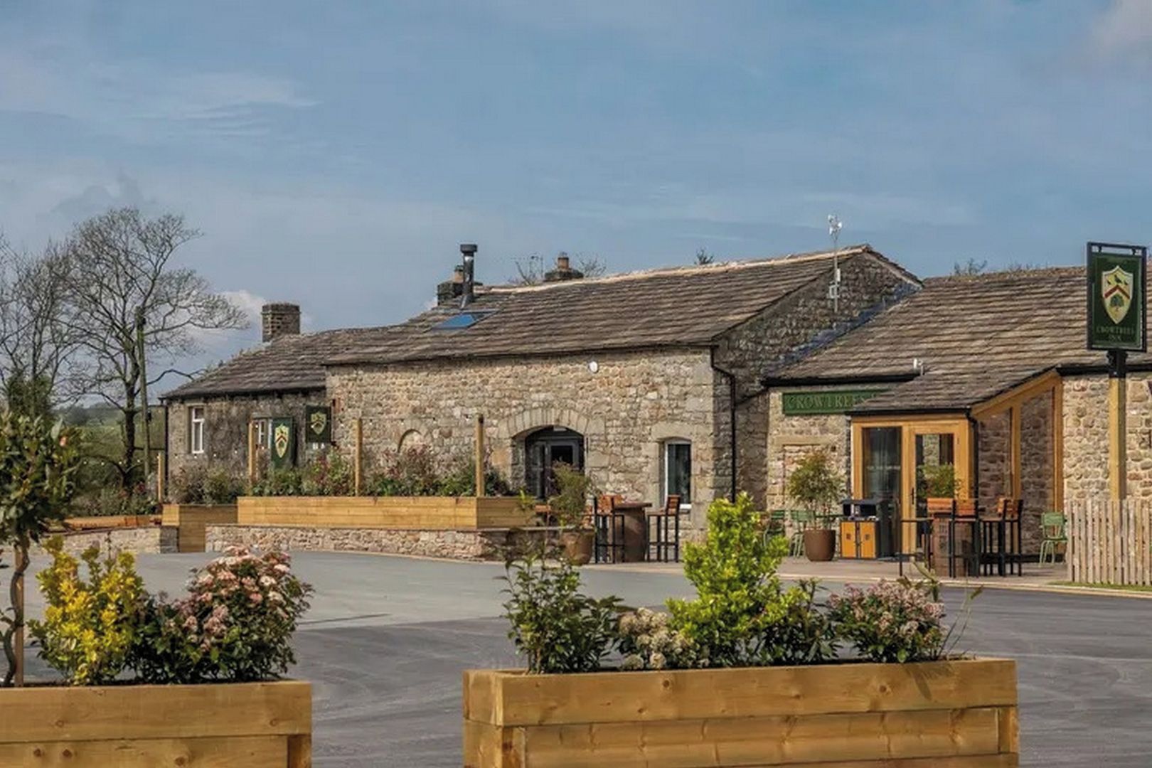 A stone building with a green sign, outdoor seating, and a paved area.