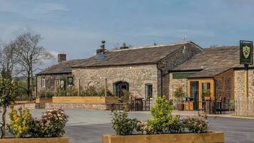 A stone building with a green sign, outdoor seating, and a paved area.