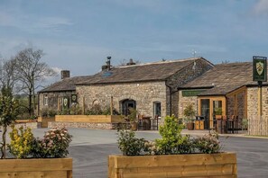 A stone building with a green sign, outdoor seating, and a paved area.