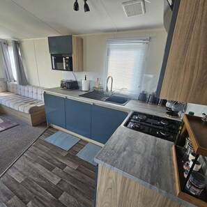 A compact kitchen with a built-in stove, a sink, and a microwave. - 3BR Countryside Caravan up to 7 Guests (Tosside)