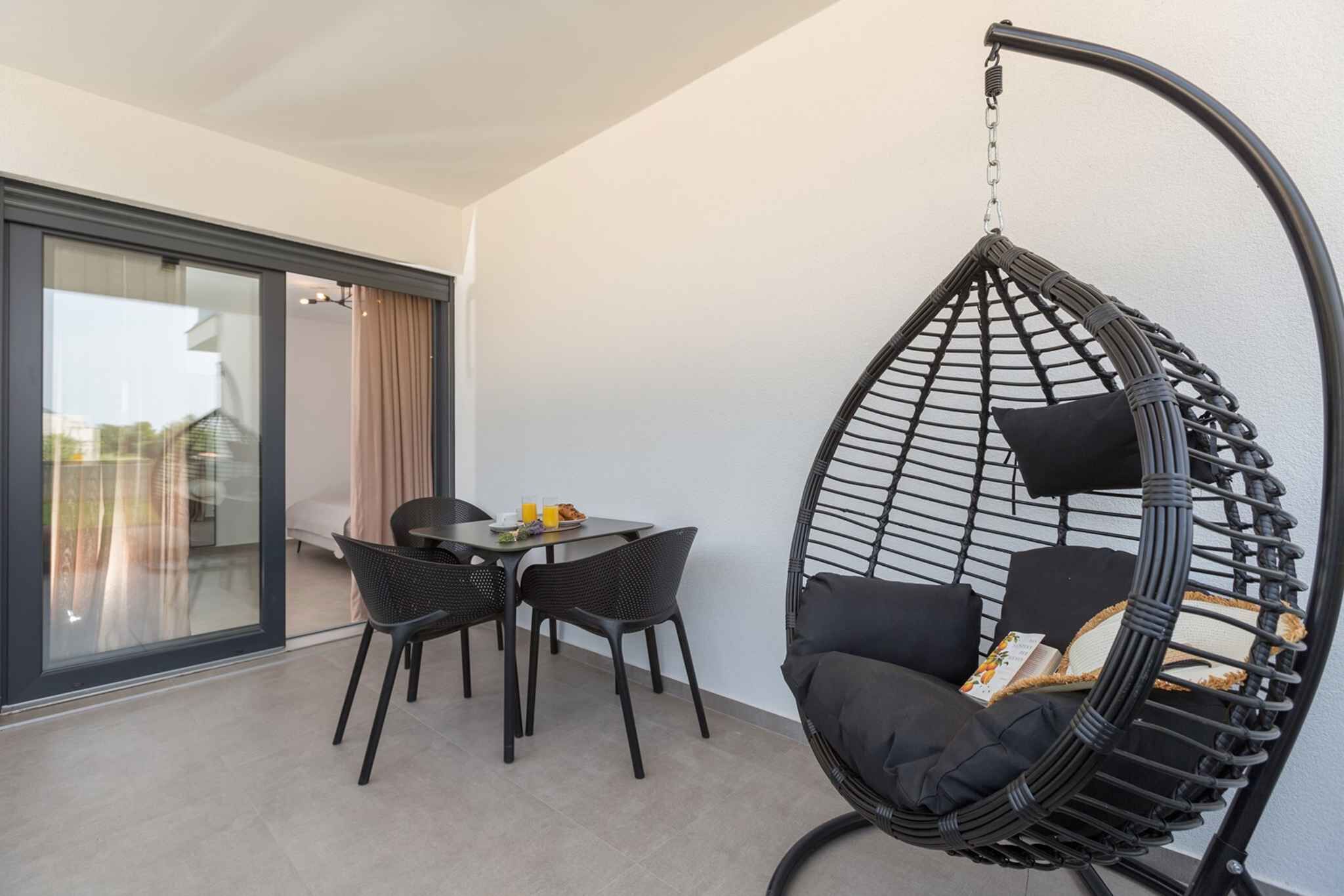 Ein moderner Balkon mit einer Hängemattenstuhls, einem Esstisch mit Stühlen und einer Glastür zum Zimmer.