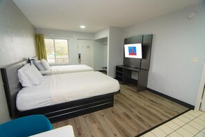 A hotel room with two beds, a TV, a desk, and a window.