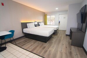 A hotel room with two beds, a desk, a chair, a TV, and a door.