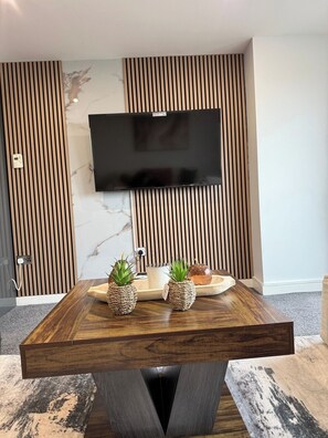 Ein modernes Wohnzimmer mit Couchtisch aus Holz, einem an der Wand befestigten Flachbildfernseher und einer Marmor-Spritzschutzwand.