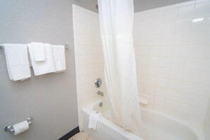 A bathroom with a bathtub, a shower curtain, and a towel rack with multiple towels.