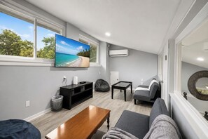 A modern living room with a TV, seating, and a view of the outdoors.