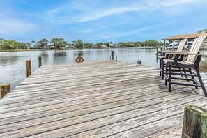 A wooden pier extending into calm water, with a lifebuoy and a row of chairs on the right.
