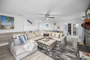 A spacious living room with a sectional sofa, a ceiling fan, and a view into the kitchen.