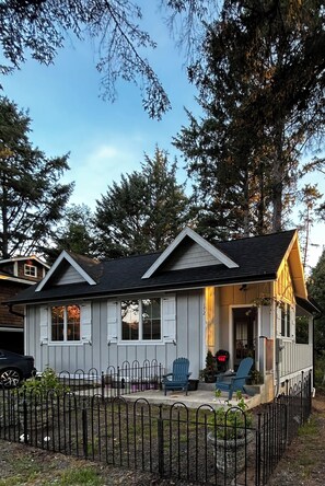 Ein eingeschossiges Haus mit Veranda, zwei blaue Adirondack-Stühle und einem eingezäunten Garten.