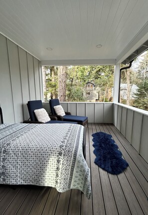 Ein überdachter Balkon mit einem Bett, zwei Stühlen und einem flauschigen, blauen Teppich.