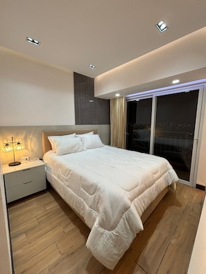 A modern bedroom with a large bed, bedside tables, a nightstand, and a view through a sliding glass door. - Apartamento moderno en Quetzaltenango (Quetzaltenango)