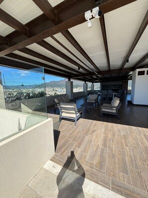A spacious outdoor area with a view of a cityscape and mountains, featuring a dining table and chairs, and a seating area with cushions. - Apartamento moderno en Quetzaltenango (Quetzaltenango)