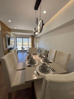 A modern dining area with a long table set for six, a television, and a balcony with a view. - Apartamento moderno en Quetzaltenango (Quetzaltenango)