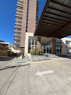 A modern building with a prominent brick tower, a covered entrance, and a clear pathway leading to the entrance. - Apartamento moderno en Quetzaltenango (Quetzaltenango)