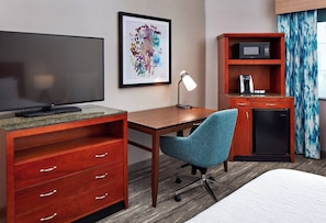 Ein Hotelzimmer mit Fernseher, Schreibtisch, Stuhl, Mikrowelle, Kaffeemaschine und einem Bett.